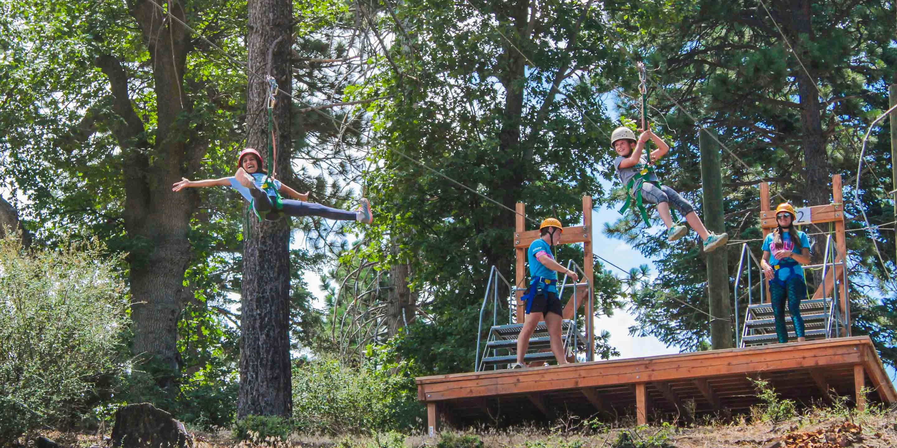 Two campers on zip line with staff in background