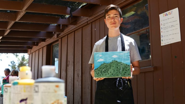 a boy holding a painted picture of green hills and foliage